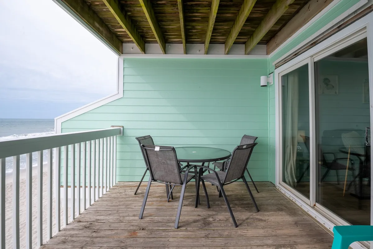 This exterior image showcases a glass table and metal chairs set on a balcony with an expansive ocean view. The tranquil scene is perfect for enjoying a sunrise or unwinding in the evening while feeling the coastal breezes.