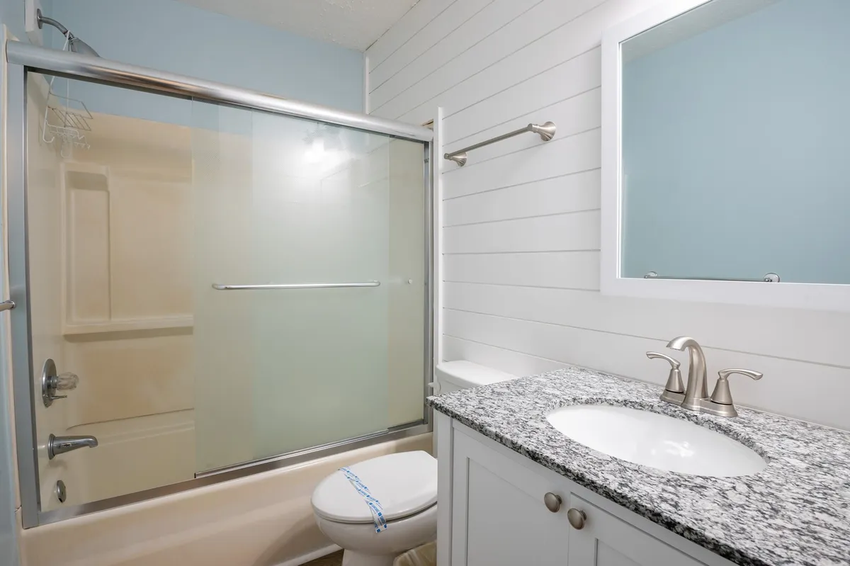 A modern bathroom featuring a sleek granite countertop, large mirror, and a glass-enclosed shower. The atmosphere is inviting and serene, ideal for personal grooming and relaxation after a day at the beach.