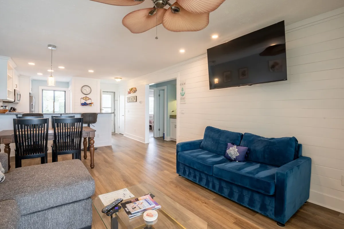 Here, a blue couch is paired with a dining table, television, and ceiling fan in a spacious, open-plan living and dining area. The setup encourages relaxation and group activities, making it an ideal gathering space for meals, movie nights, and shared moments.