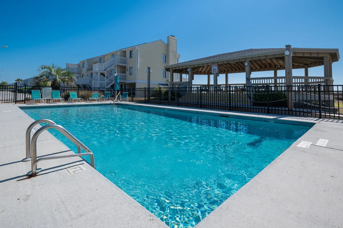 An inviting outdoor pool area surrounded by lounge chairs and a gazebo, with clear skies and a tranquil atmosphere. The pool is spacious, ideal for families to swim, sunbathe, and relax together.