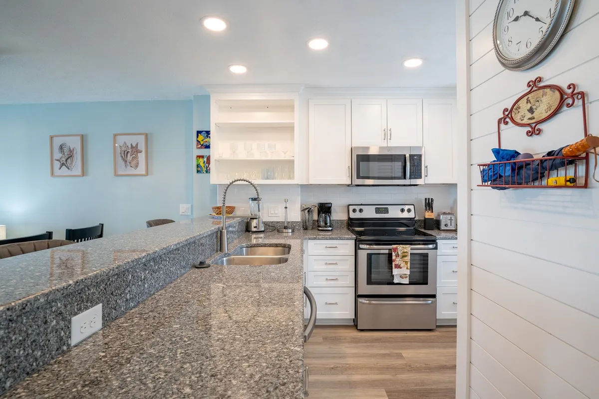 A welcoming and functional kitchen with a granite countertop, stainless steel appliances, white cabinetry, and decorative wall art. The open layout promotes shared cooking experiences and family gatherings, with plenty of space for meal prep and entertaining.